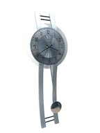 A modern wall clock with a silver metallic circular face and a matching silver pendulum, mounted on a white wall.
