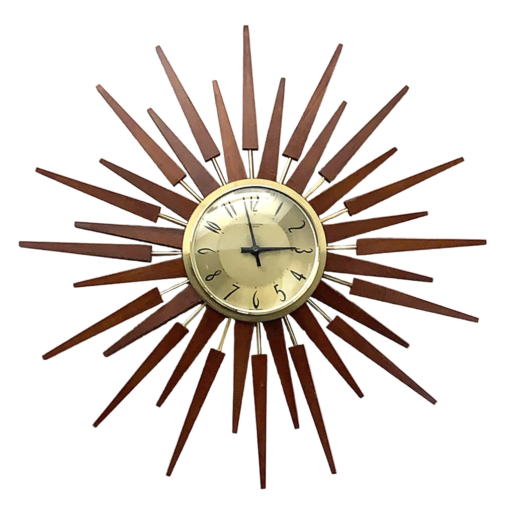 A mid-century modern sunburst wall clock with a circular beige dial, black hands, and a surrounding frame made of multiple radiating wooden rays in warm brown tones.