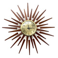 A mid-century modern sunburst wall clock with a circular beige dial, black hands, and a surrounding frame made of multiple radiating wooden rays in warm brown tones.