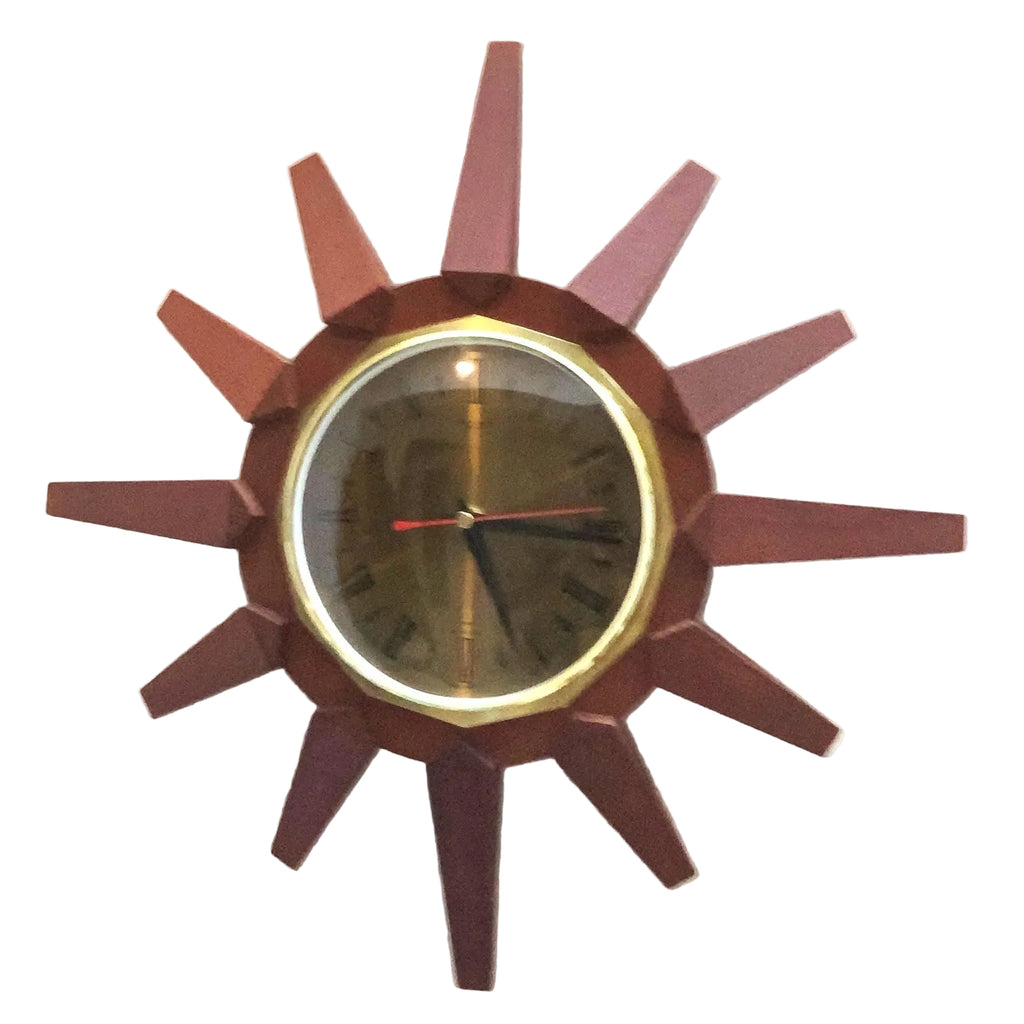 A mid-century modern sunburst wall clock with a dark reddish-brown geometric wooden frame, a gold-tone bezel, and a dark dial with black Roman numerals and a red second hand.